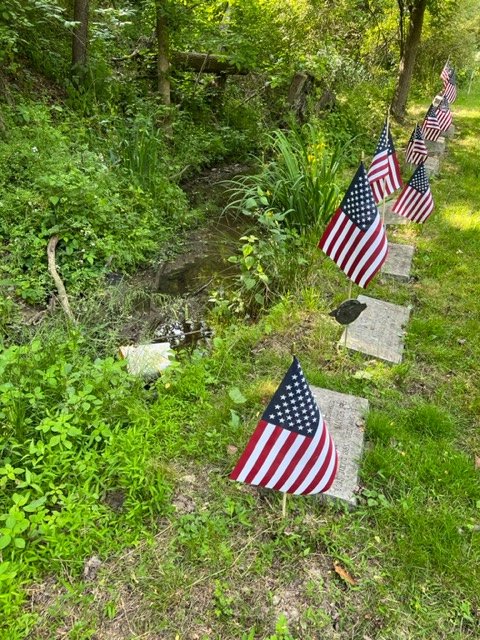 Another close view of flagged headstones near the creek.
